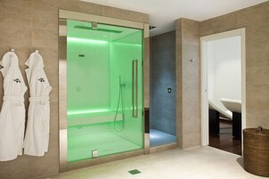 Un bagno moderno con doccia vetrata, una vasca da bagno bianca e due accappatoi bianchi appesi al muro.