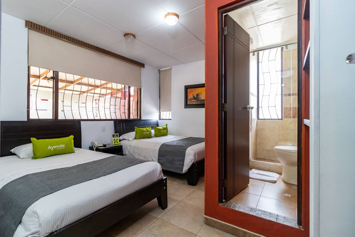 Una habitación de hotel con dos camas, un baño y vistas por una ventana.