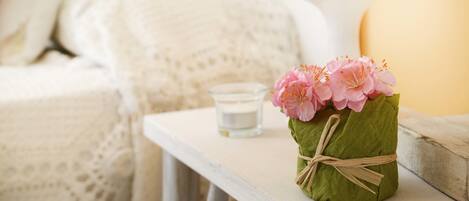 A cozy room with a white bed, a small table with a candle and a vase of flowers.