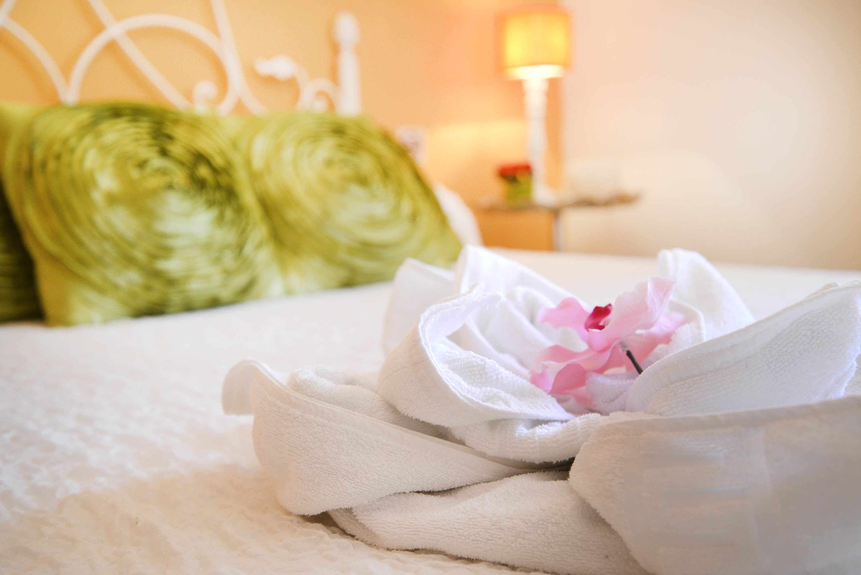 A neatly made bed with a white towel and a pink flower.