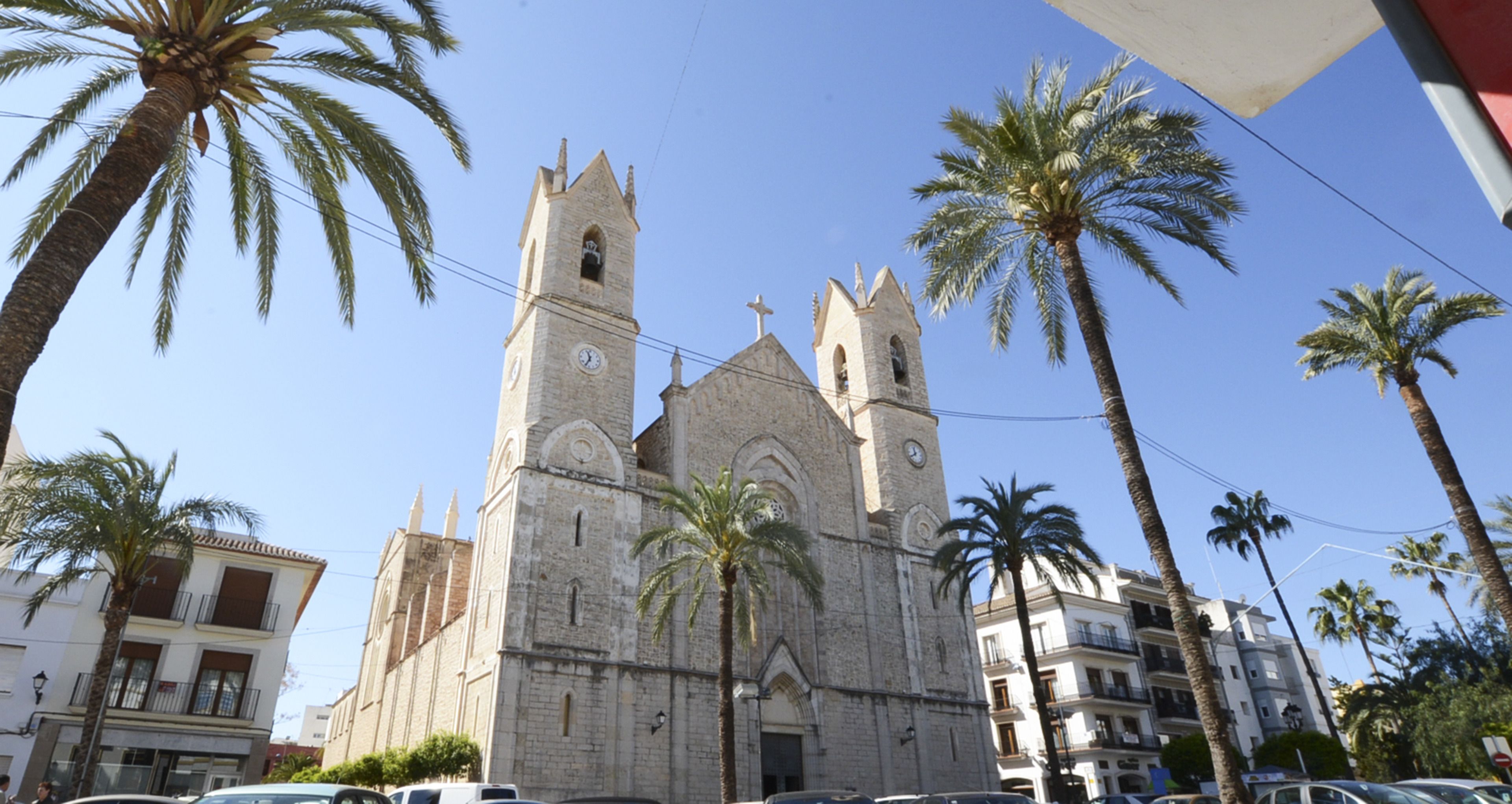 Una iglesia histórica con dos torres y un reloj, rodeada de palmeras y edificios modernos.