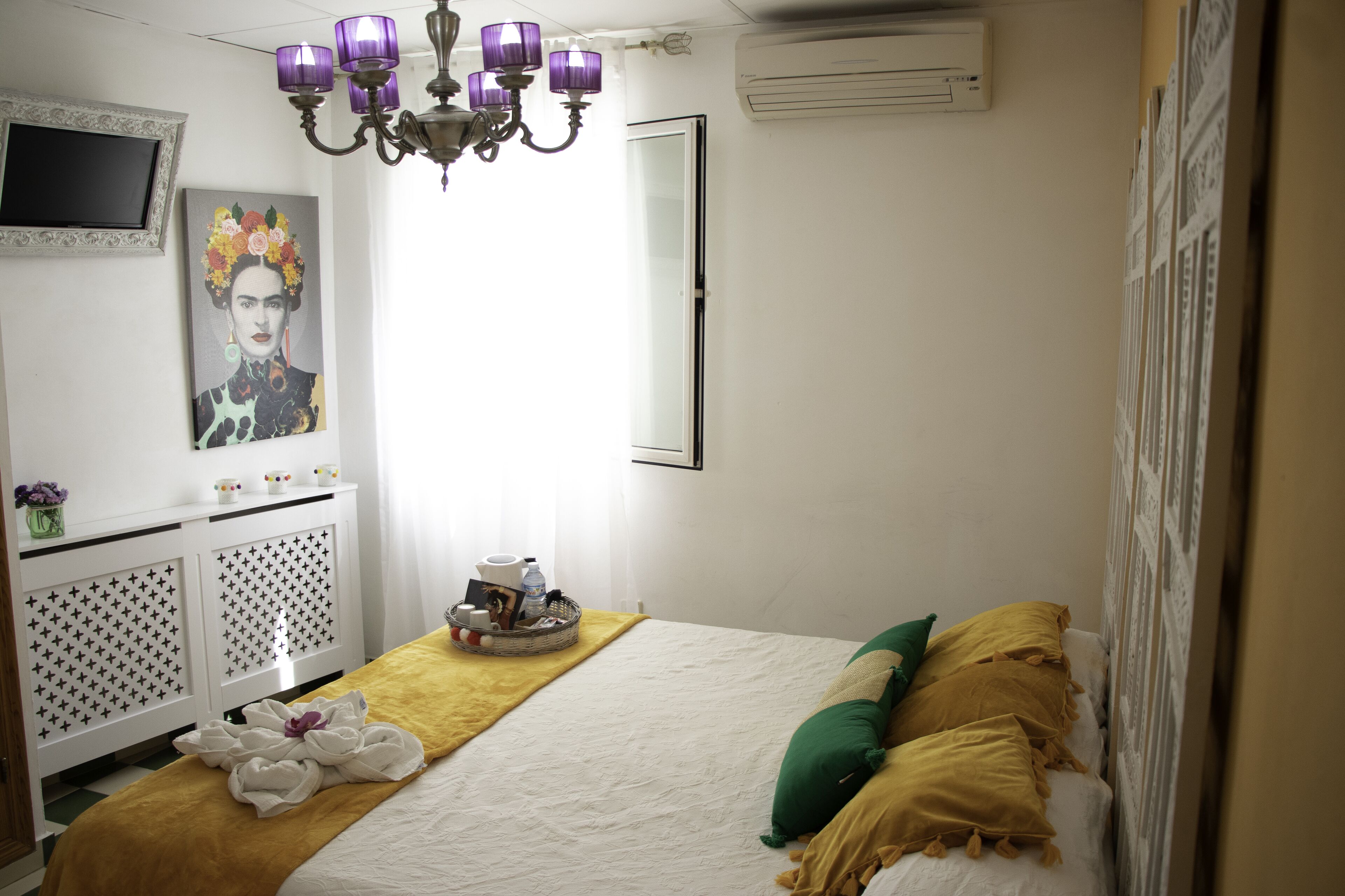 A neatly arranged hotel room with a bed, a bedside table with a lamp, a wall-mounted TV, and a window with curtains.