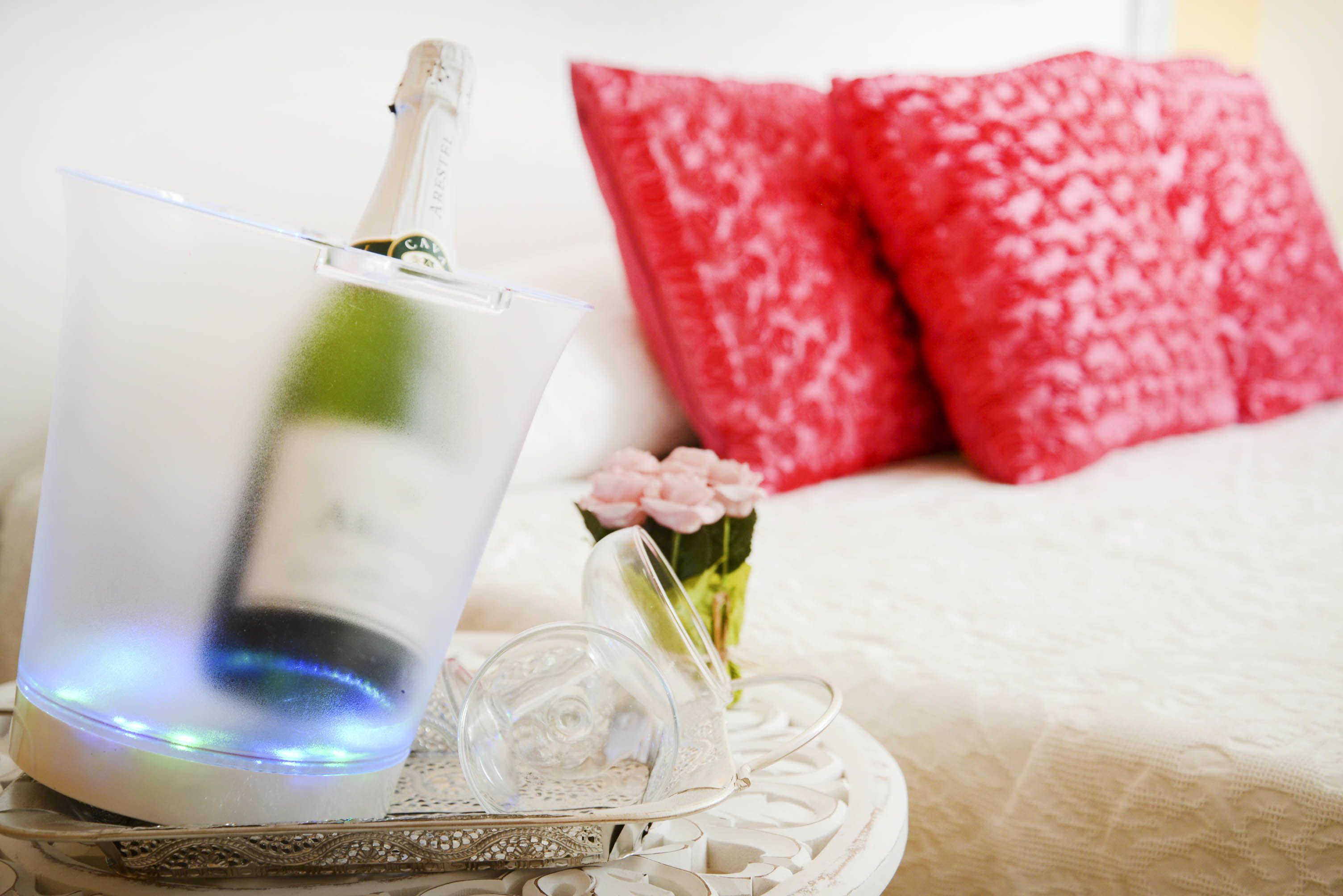 Un vaso transparente con luz azul, una botella blanca y una bandeja decorativa con una campana de vidrio y un pequeño florero con flores rosadas.