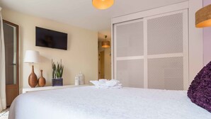 A hotel room with a bed, a wall-mounted TV, a window with curtains, a bedside table with a lamp, a vase, and a potted plant. - Terra de Mar Boutique Calpe (Calpe)