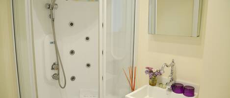 A bathroom with a glass-enclosed shower, a white sink with a mirror above it, and a small vase with flowers on the sink.