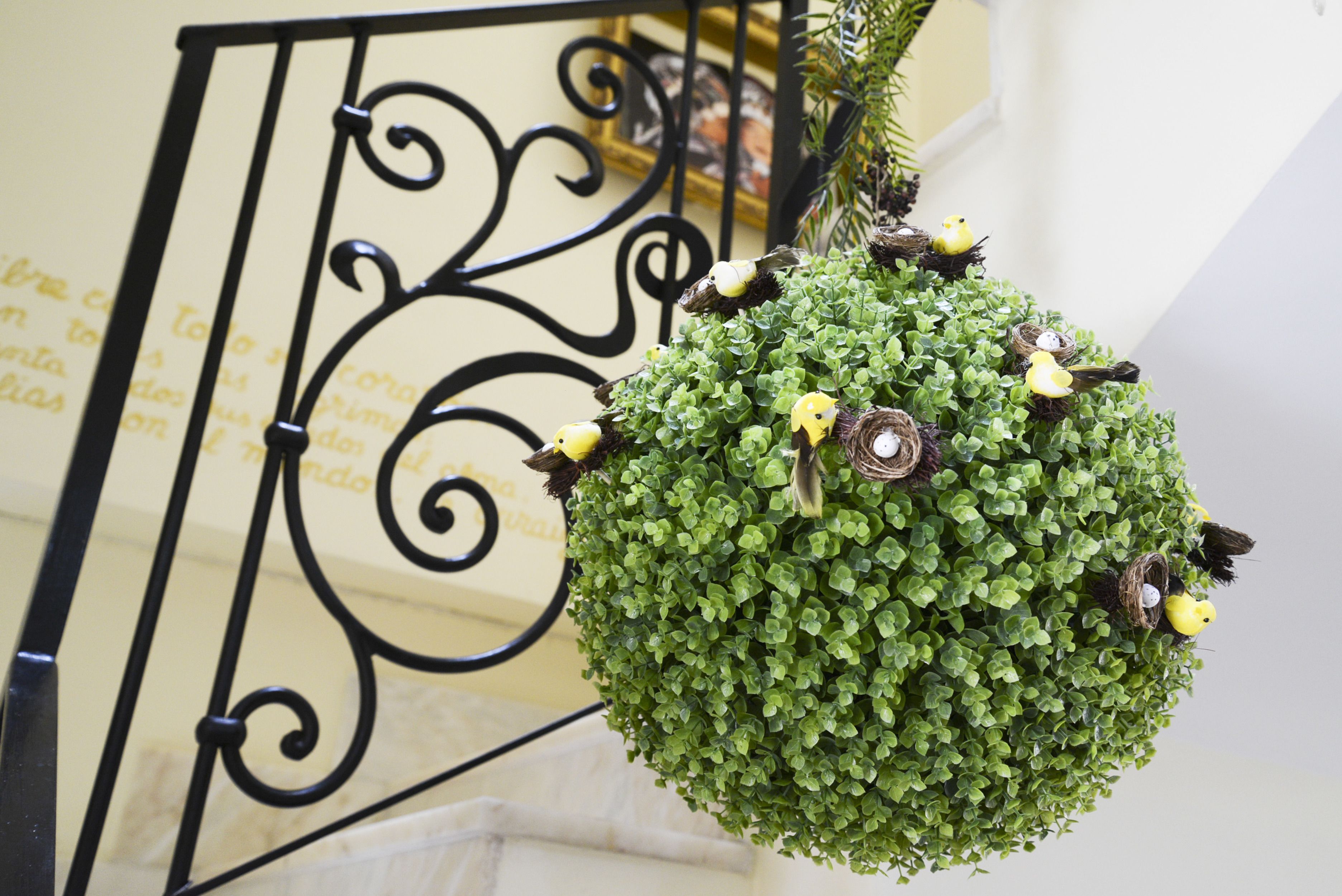 A hanging green plant with bird figurines and a decorative metal railing.