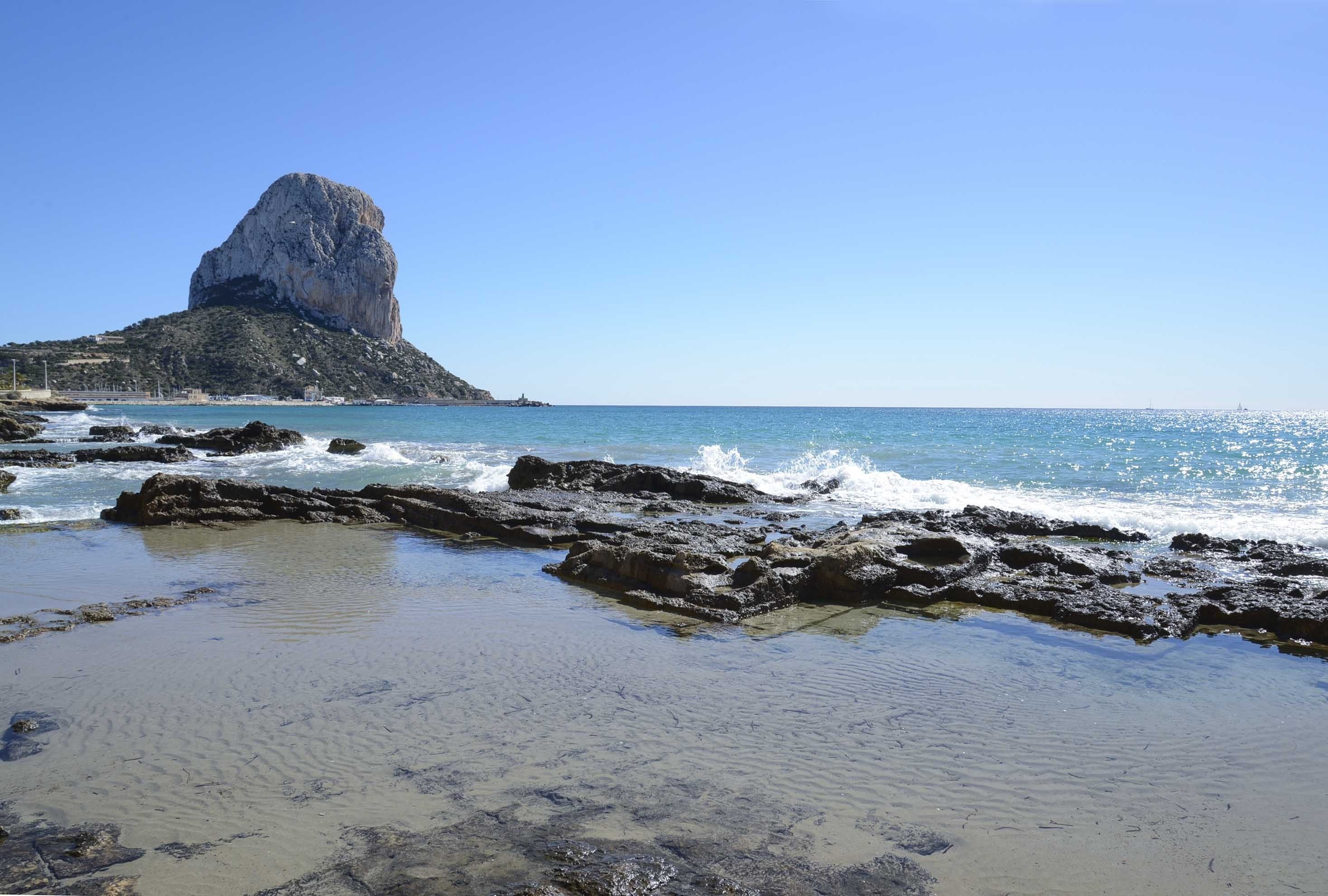 Uma praia rochosa com águas azul-claras e uma formação rochosa imponente.