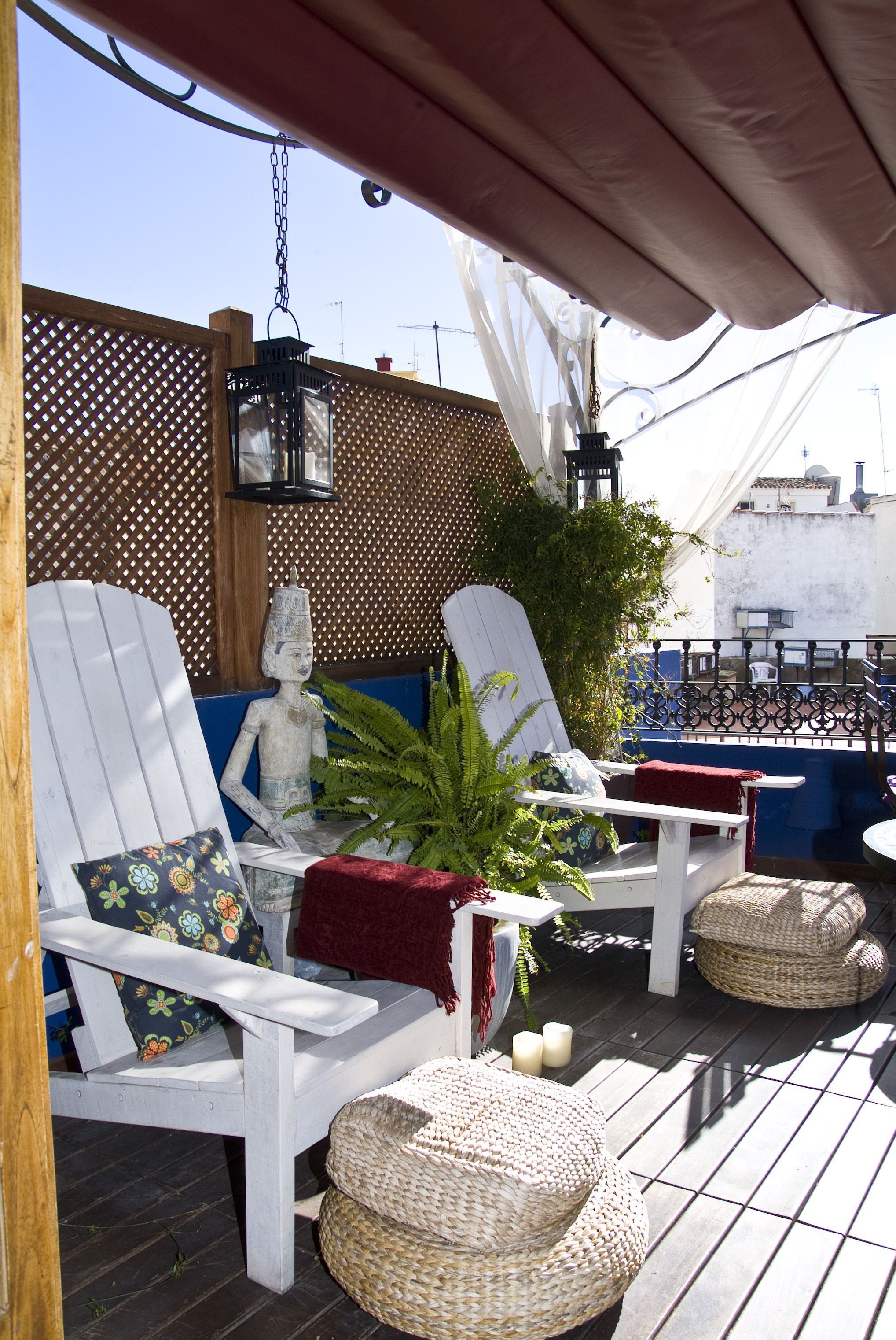 A covered outdoor seating area with white chairs, wicker ottomans, and a decorative plant.