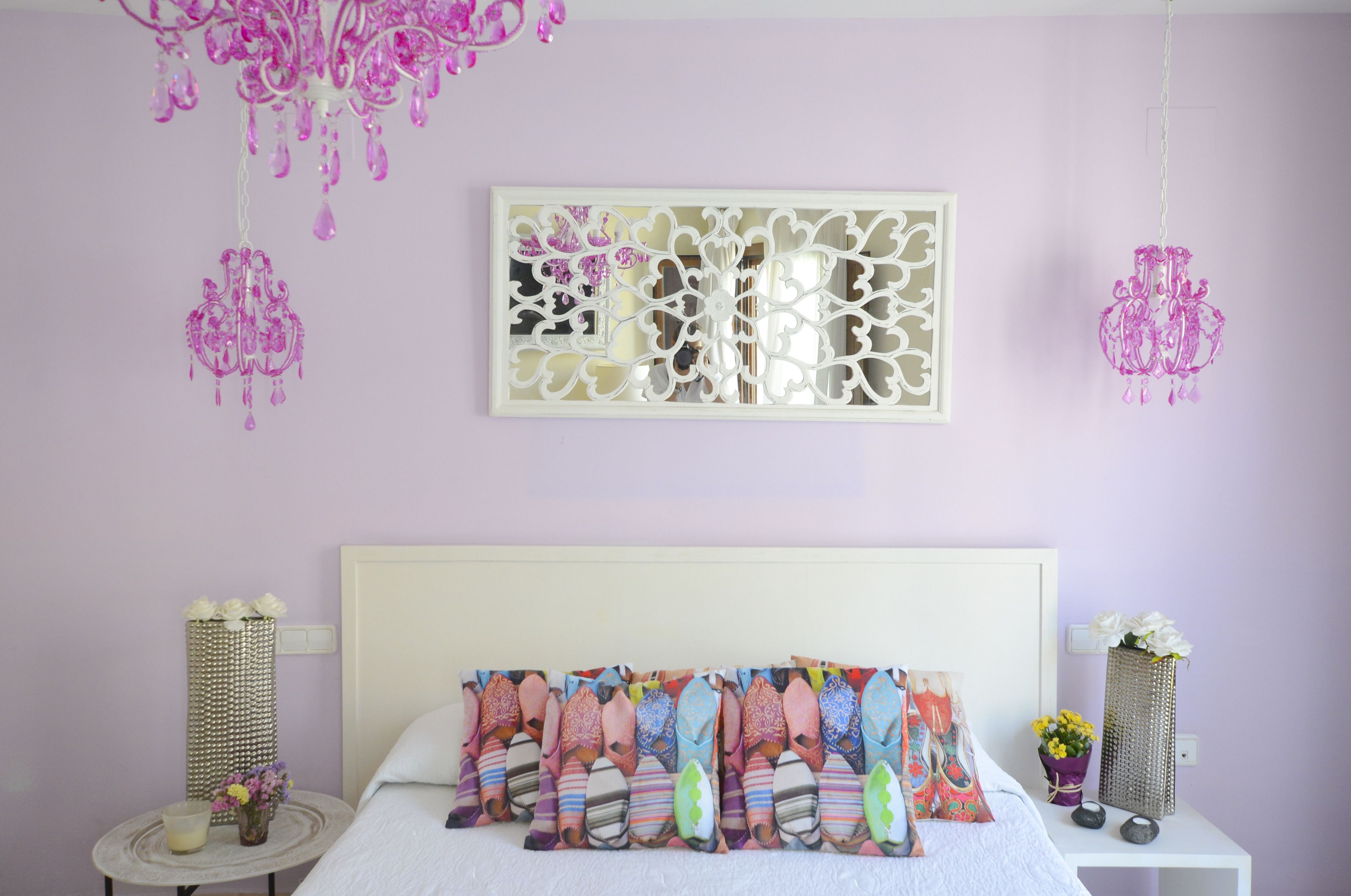 Un dormitorio con cama blanca, almohadas decorativas, cabecera blanca y un panel decorativo en la pared.