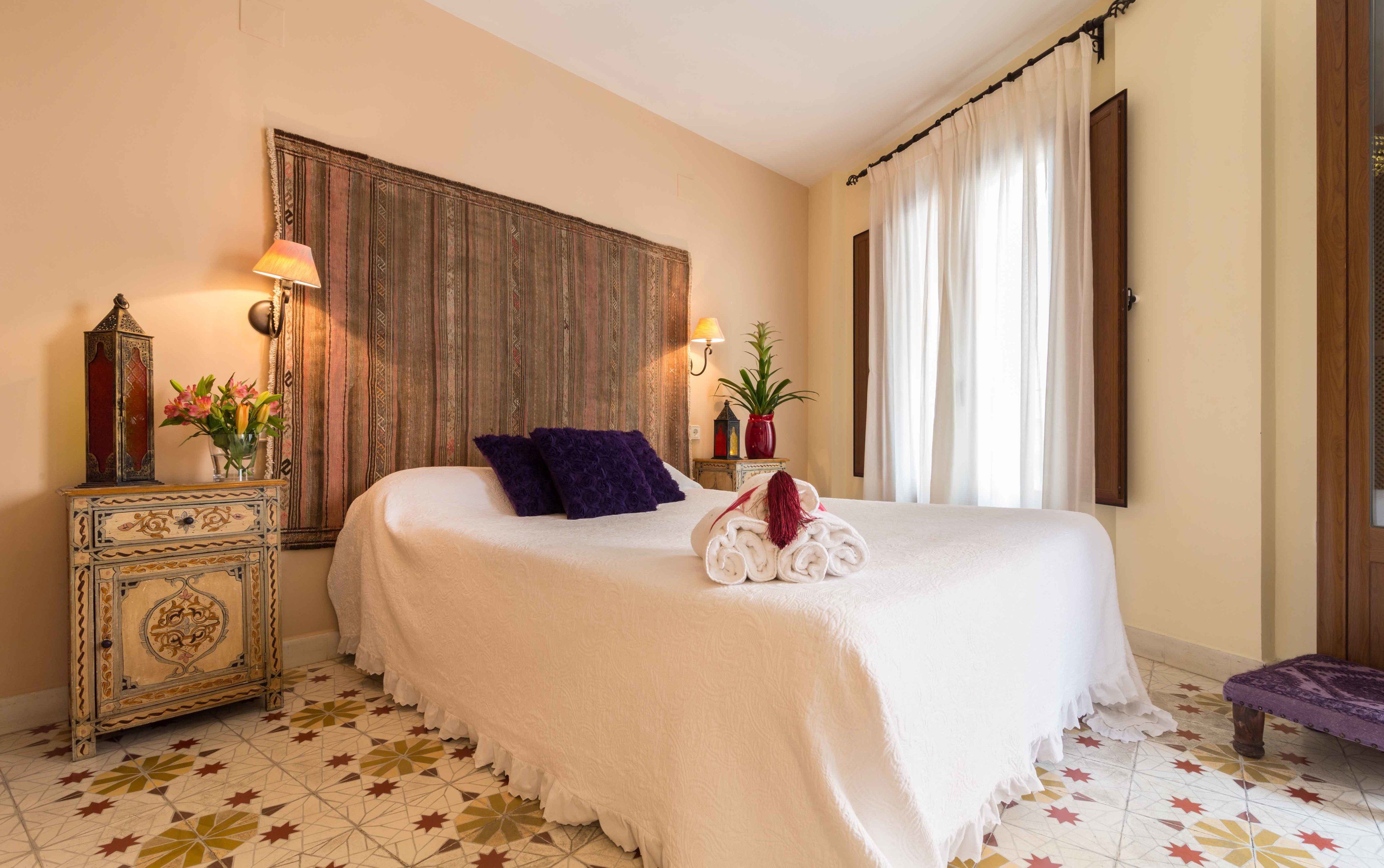 A hotel room with a large bed, a decorative cabinet, a wall-mounted lamp, and a potted plant.