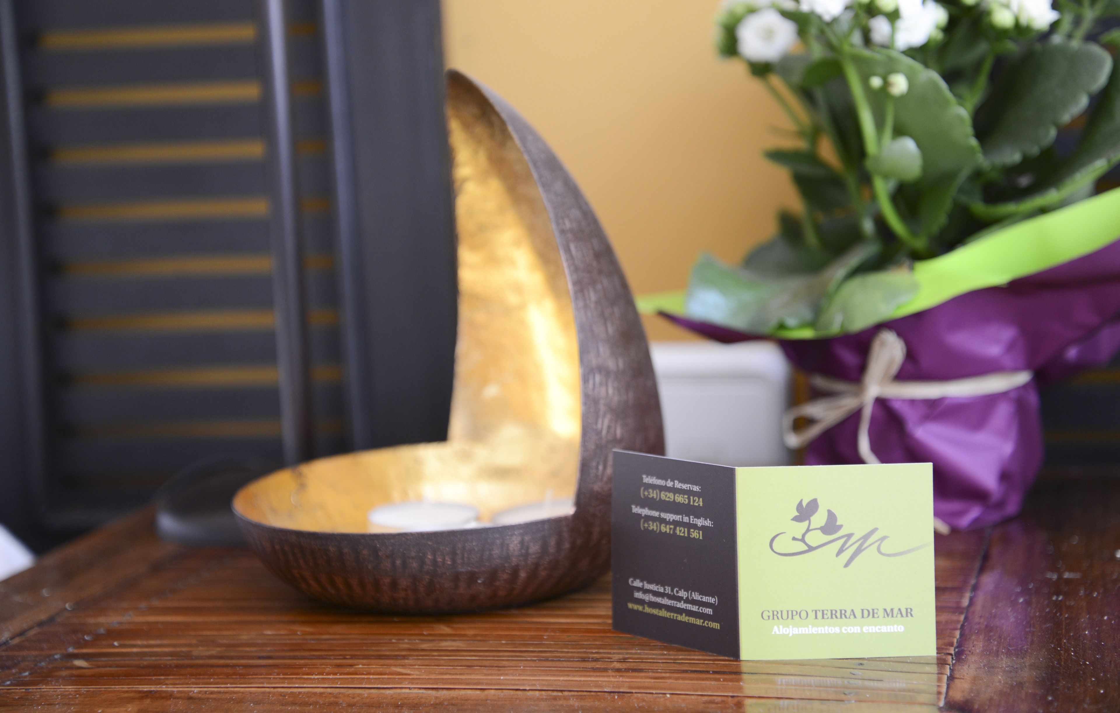 A wooden bowl with candles, a business card, and a purple gift bag on a wooden table.