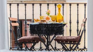 A table set with a fringe tablecloth, two cushioned chairs, and various items including a yellow bottle, a glass, and a small vase with flowers.