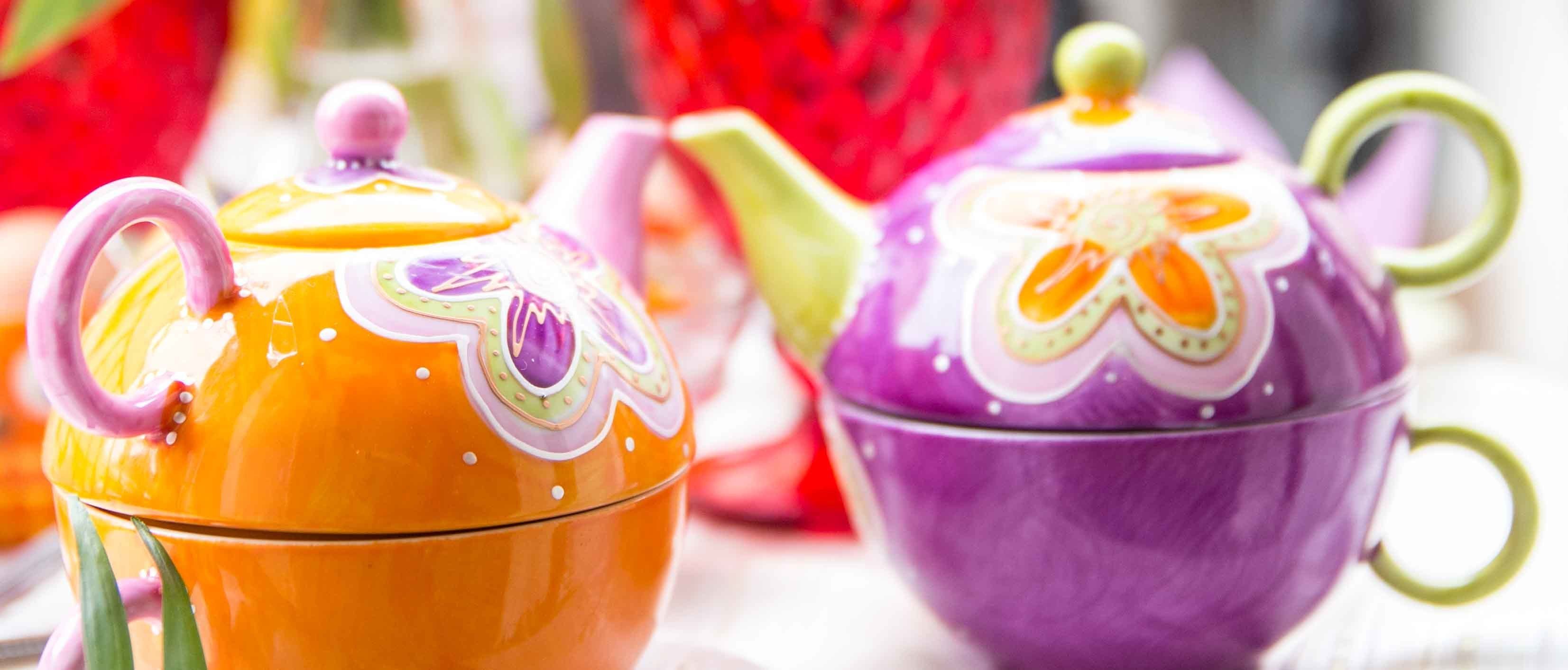 Dos teteras de cerámica coloridas, una naranja y otra morada, con diseños decorativos.