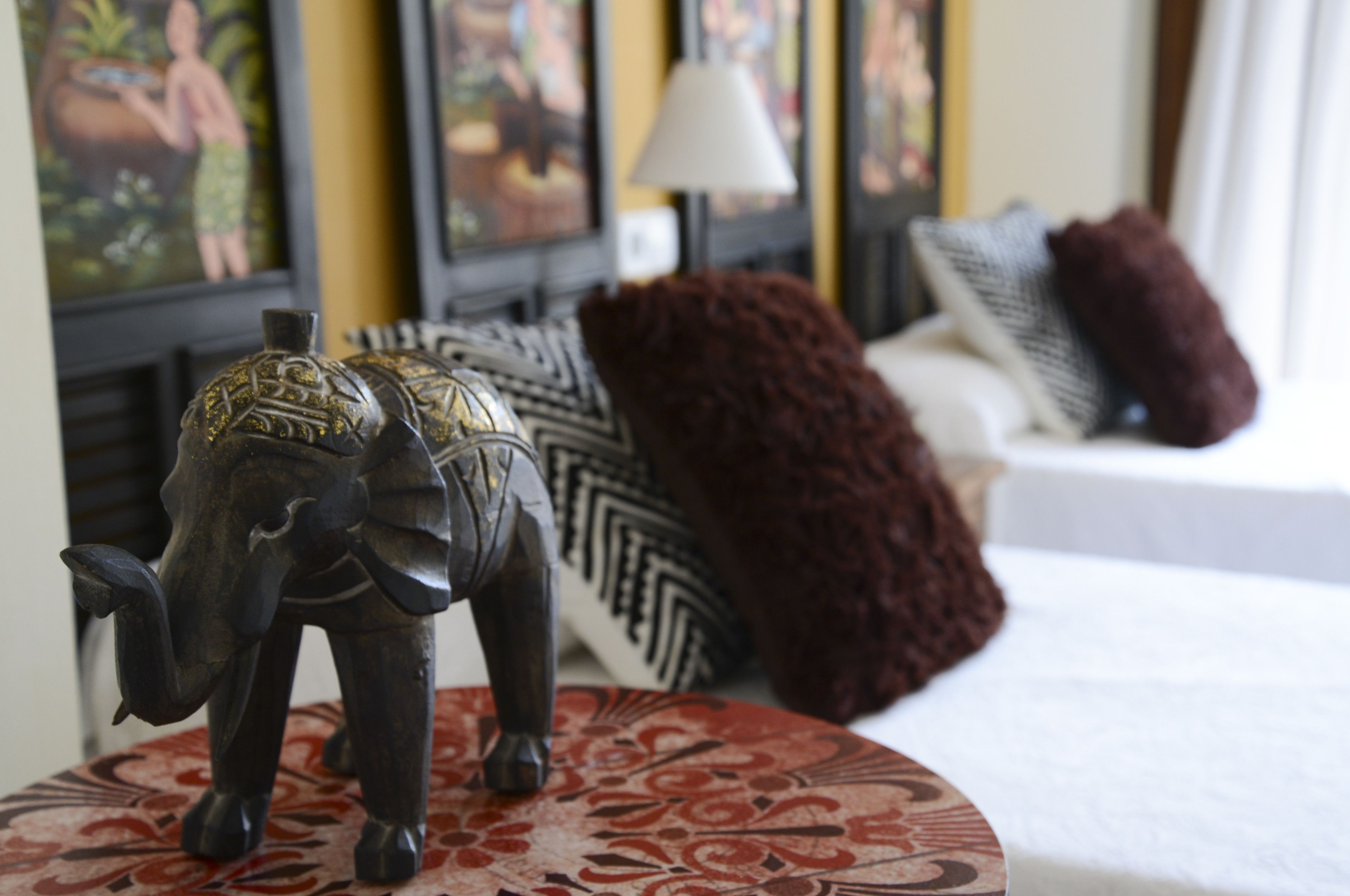 A bed with a decorative elephant head, a patterned table, and a sofa with pillows.