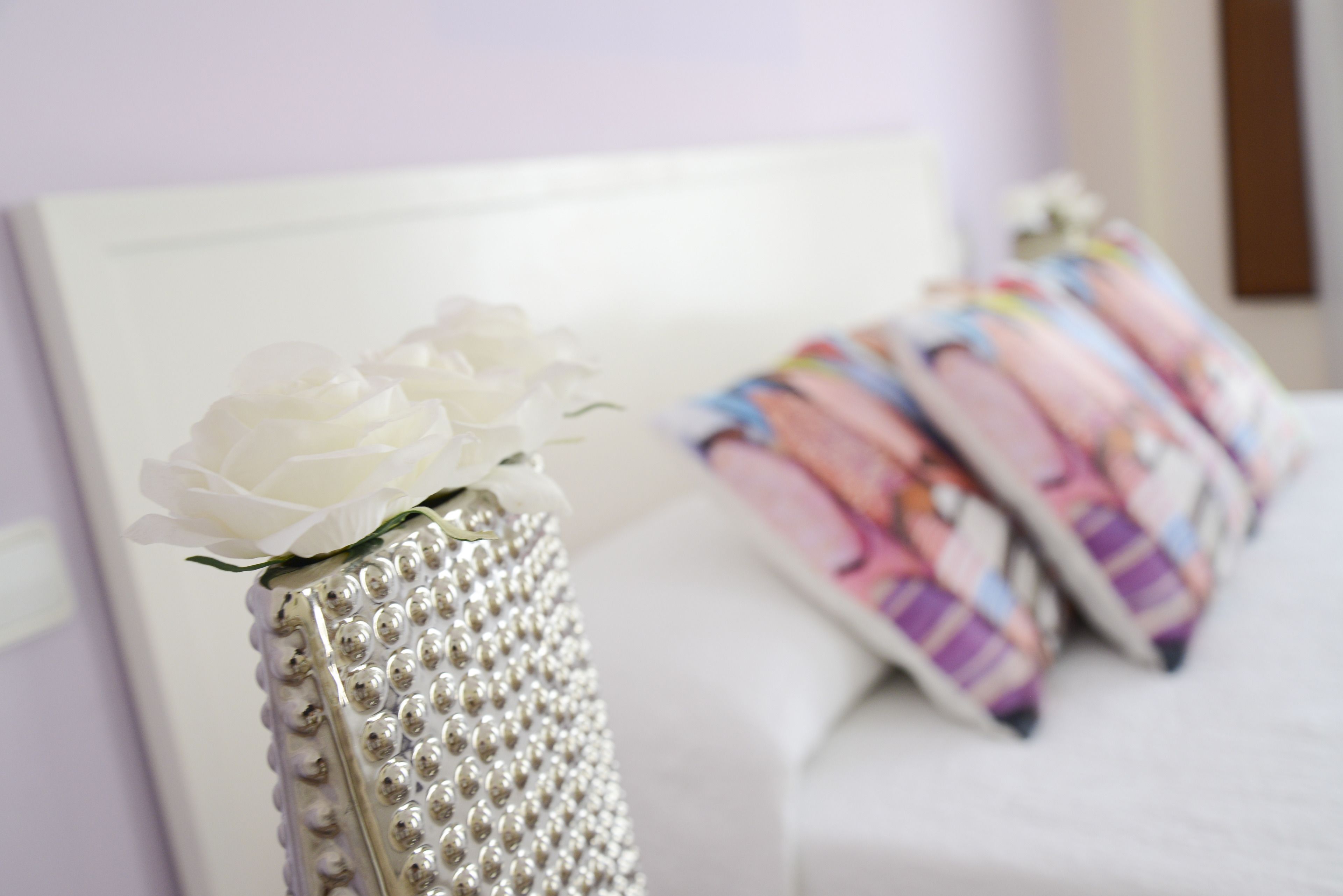 A bed with a white headboard and a decorative vase with white flowers.