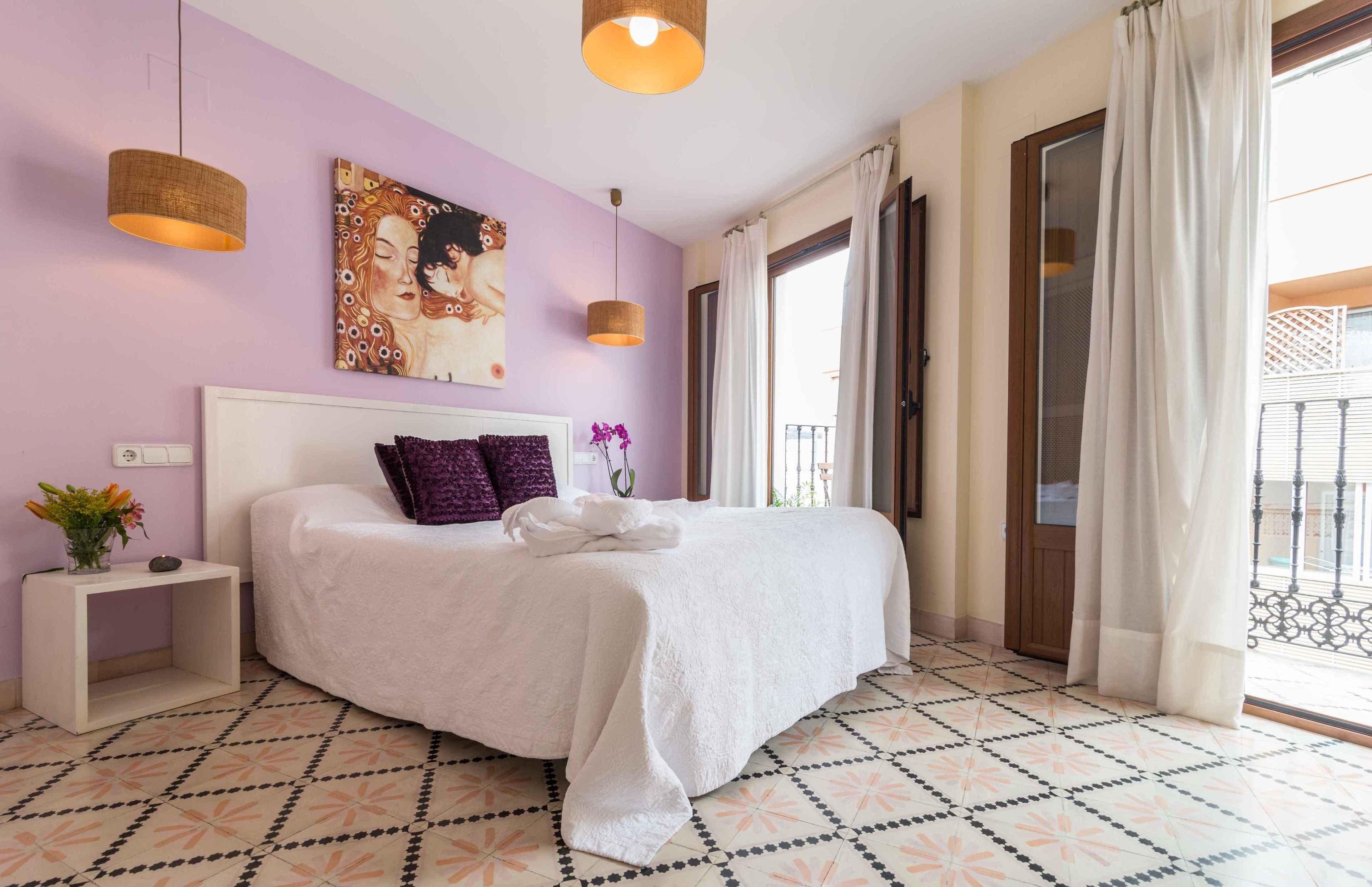 Une chambre à coucher avec un lit, une table de chevet, un tableau et une fenêtre avec des rideaux.