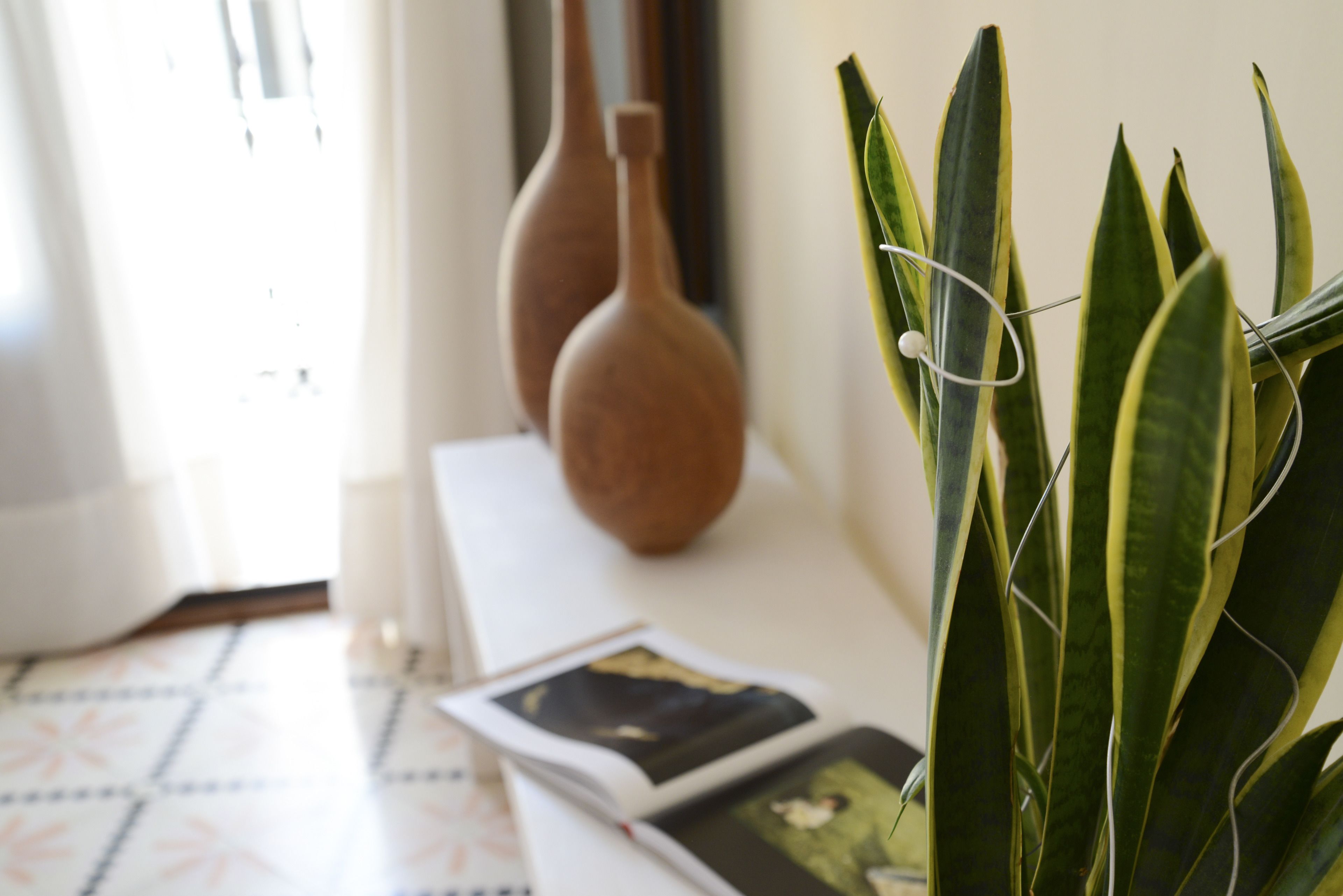 A room with a tiled floor, a white table with two vases, and a potted plant.