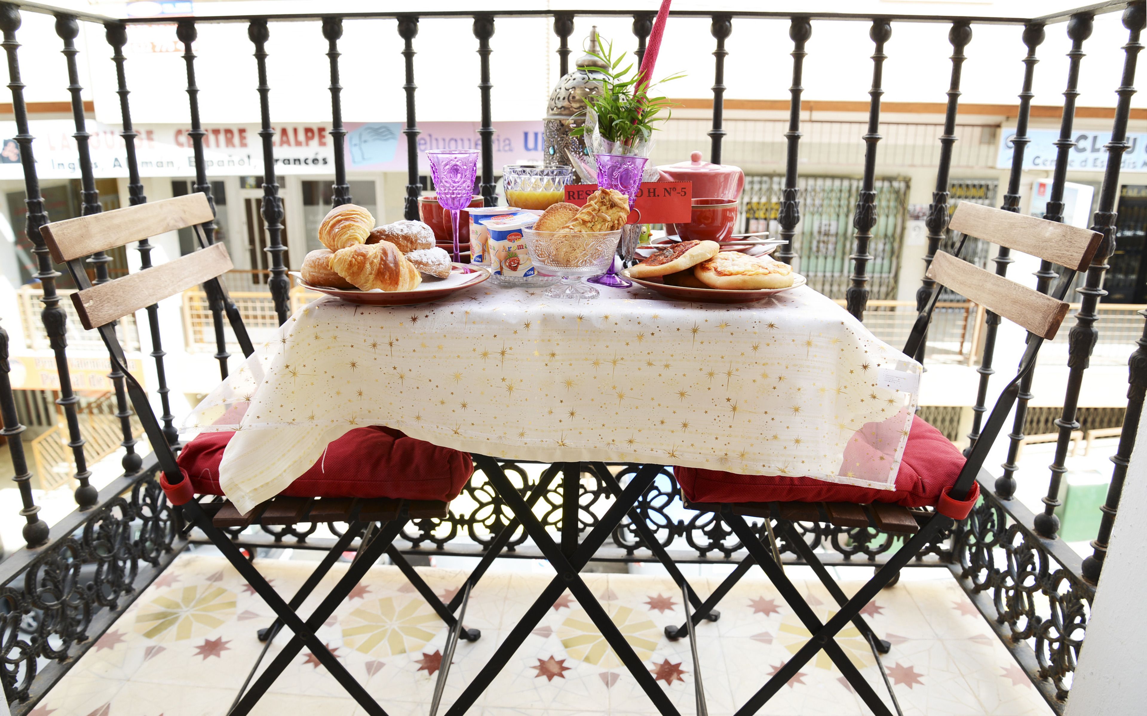 Una mesa servida con pasteles y un vaso de jugo en un balcón con barandillas negras ornamentadas.
