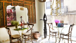Una habitación con un espejo grande y ornamentado, sillas de madera, una pequeña mesa redonda con una planta en maceta y un jarrón decorativo.