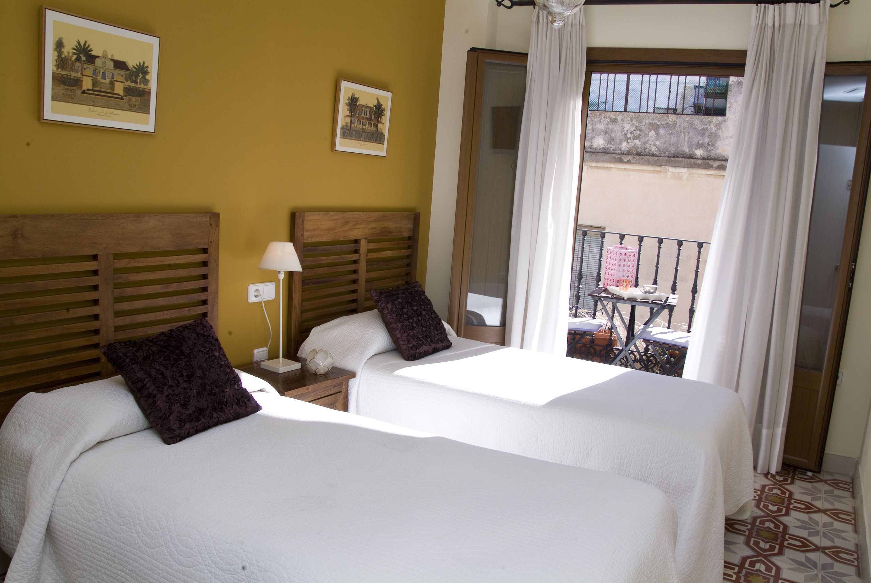 A hotel room with two beds, a nightstand, a lamp, and a balcony with a table and chairs.