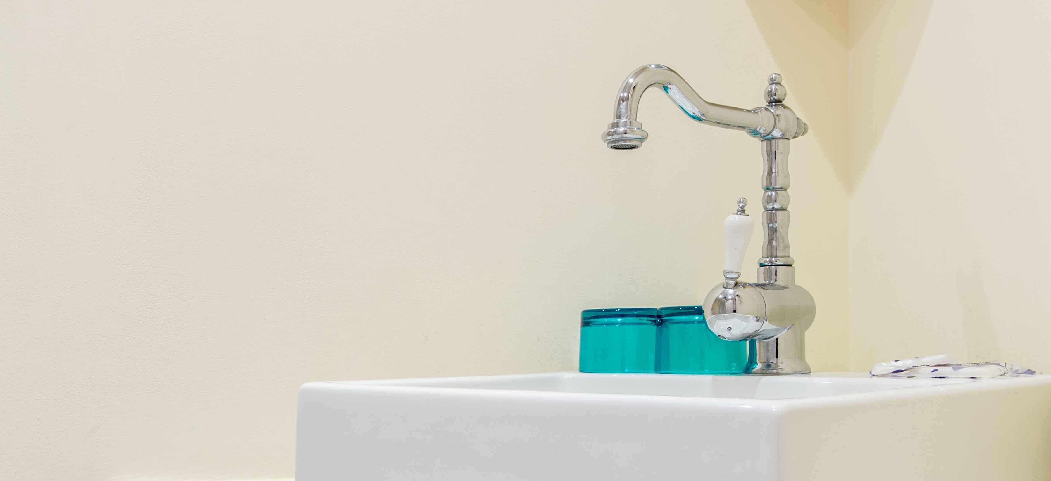 A bathroom with a white sink, a chrome faucet, and a glass soap dispenser.