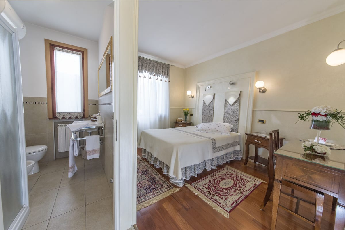 A bedroom with a bed, a bedside table, a dresser, a mirror, and a window with curtains.