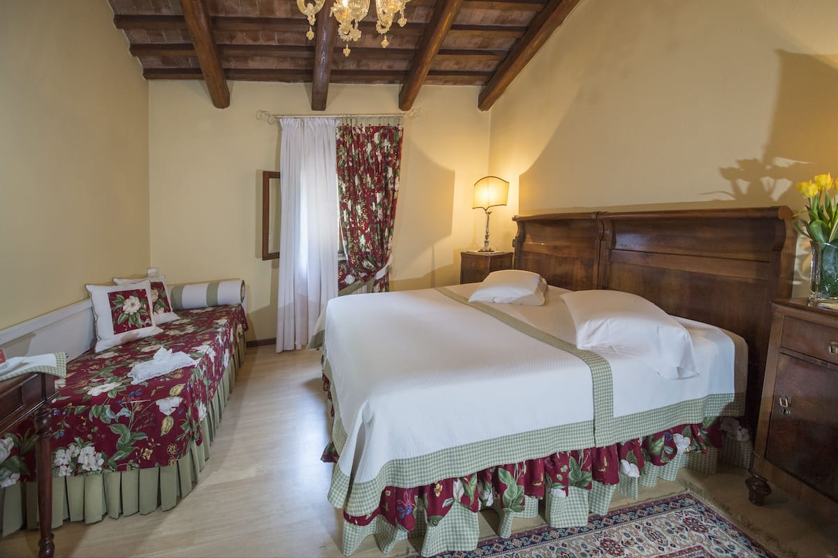 A bedroom with a large bed, a smaller bed, a nightstand, a lamp, and a wooden headboard.