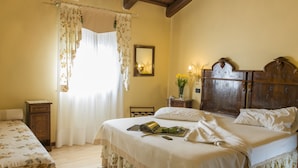 A bedroom with a wooden headboard, a bed with floral bedding, a nightstand with a lamp, and a window with floral curtains. - Hotel La Rescossa (Mira)