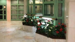 Un vestíbulo con mostrador de recepción verde, piso de baldosas y plantas en macetas.