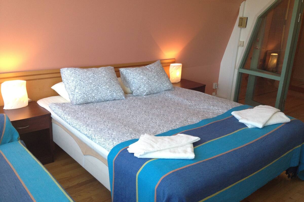 A hotel room with a large bed, two bedside tables, a nightstand, and a window with a view.
