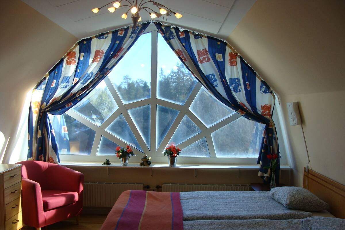 A bedroom with a large window, a bed, a chair, and a dresser.