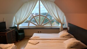 Un dormitorio con dos camas, un escritorio, una silla y un amplio ventanal con cortinas.