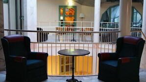 Un balcón con dos sillones y una mesita redonda, con vistas a un edificio con una puerta verde y una ventana.