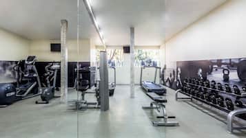 Un gimnasio con cintas de correr, elípticas, bancos de pesas y un estante de mancuernas.
