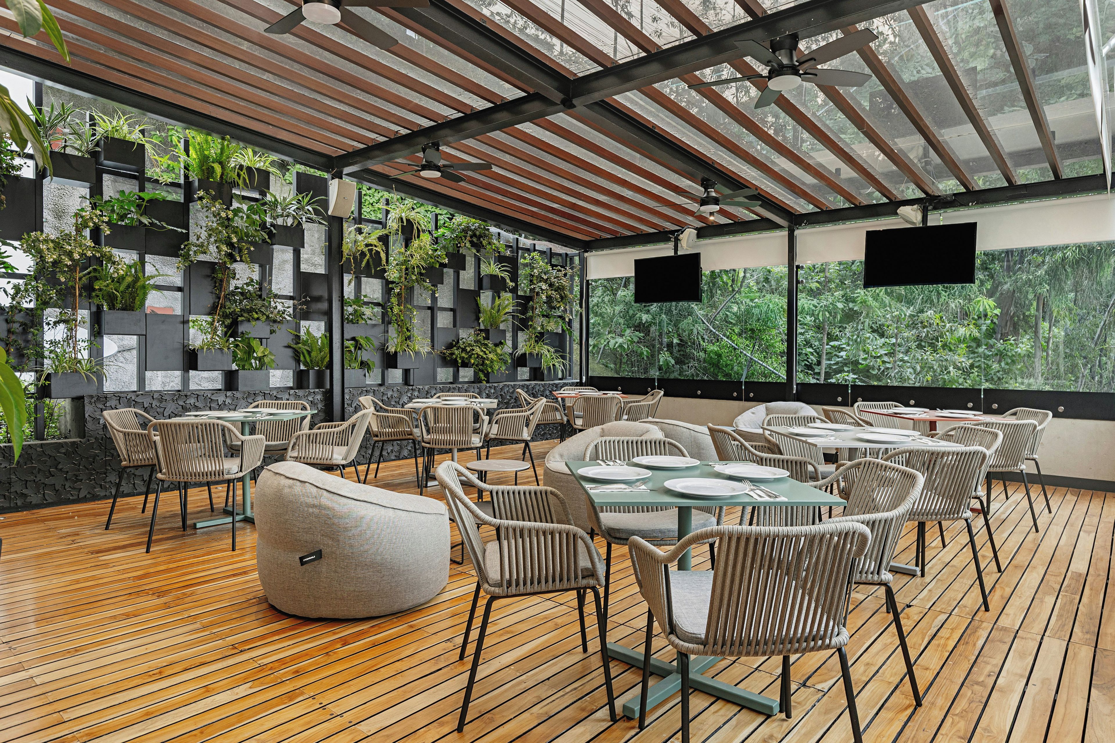 An outdoor seating area with wooden flooring, wicker furniture, and a backdrop of greenery.