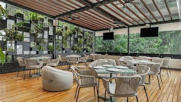 An outdoor seating area with wooden flooring, wicker furniture, and a backdrop of greenery.