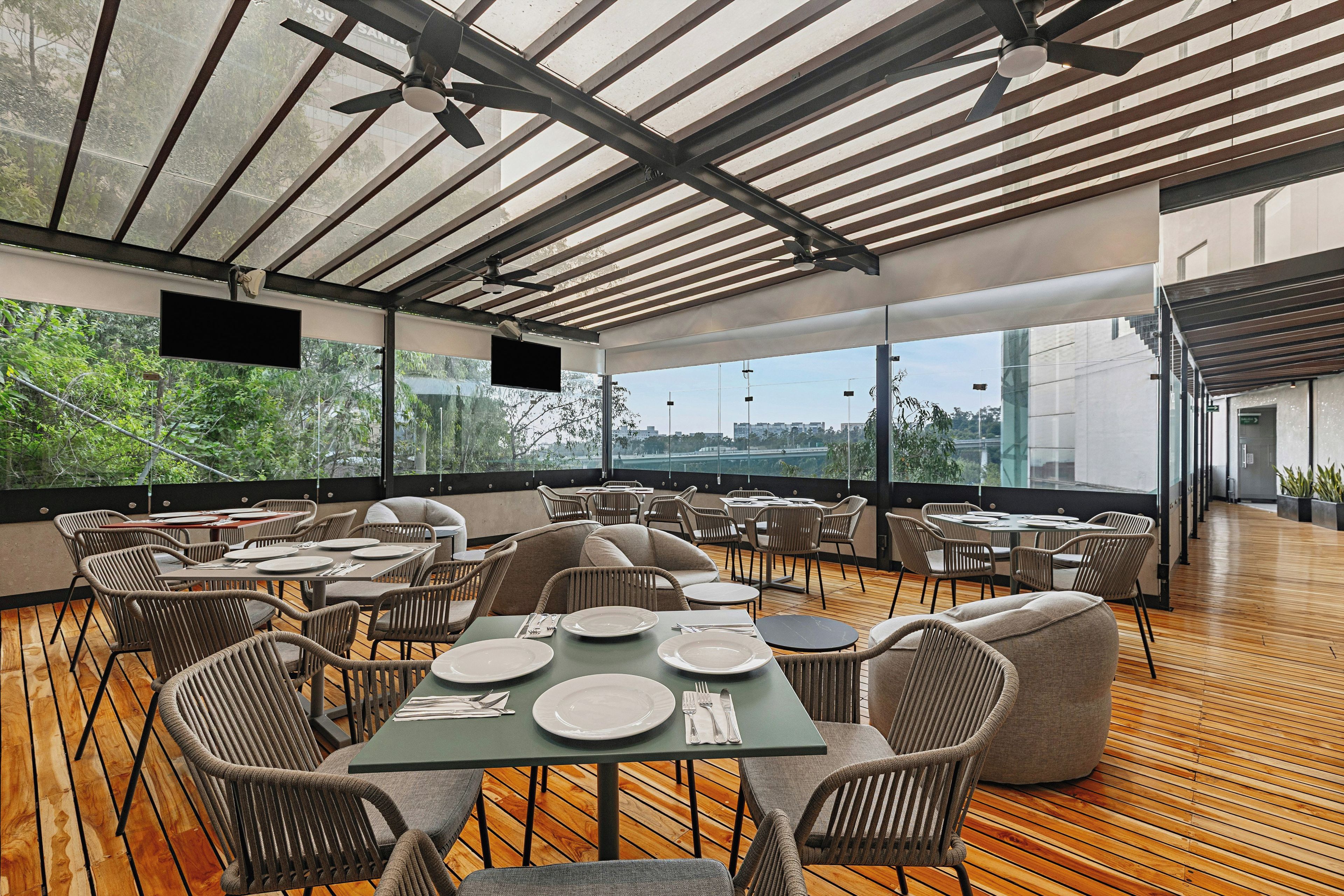 An outdoor dining area with tables and chairs, large windows, and a ceiling fan.