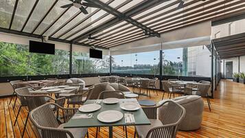 An outdoor dining area with tables and chairs, large windows, and a ceiling fan.