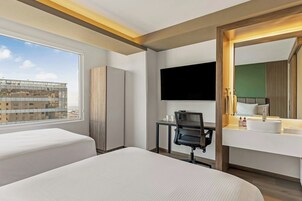 A hotel room with two beds, a desk, a chair, a TV, and a large mirror.