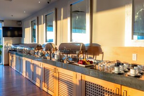 A buffet setup with multiple serving stations, a flat-screen TV, and large windows allowing natural light. - Gamma Ciudad de Mexico Santa Fe (Mexico City)