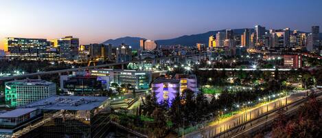 Une vue sur une ville au crépuscule, avec des bâtiments illuminés et une autoroute.