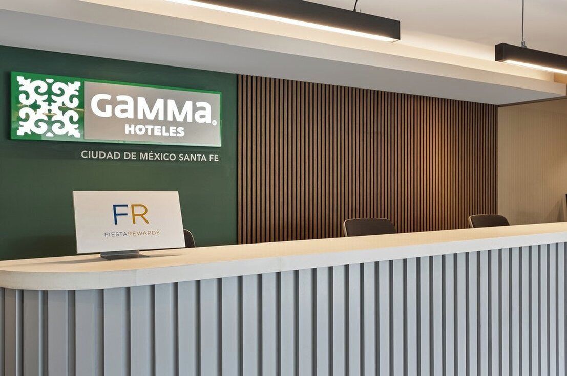 Un comptoir d’accueil d’hôtel avec une enseigne indiquant « Gamma Hotels Ciudad de México Santa Fe » et une autre enseigne indiquant « Fiesta Rewards ».