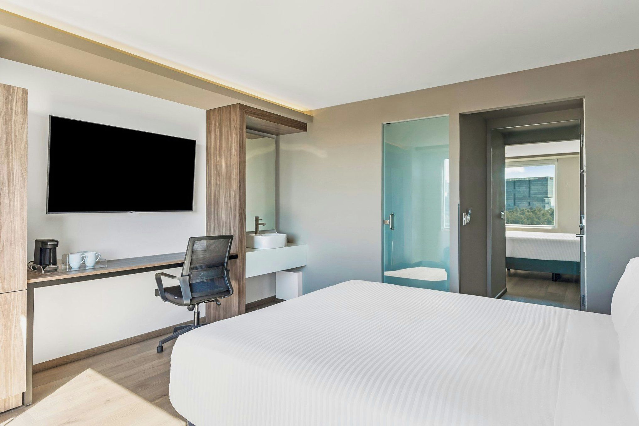 Ein Hotelzimmer mit Bett, Schreibtisch mit Stuhl, Fernseher und Badezimmer inklusive Spiegel, sowie Blick ins Freie.