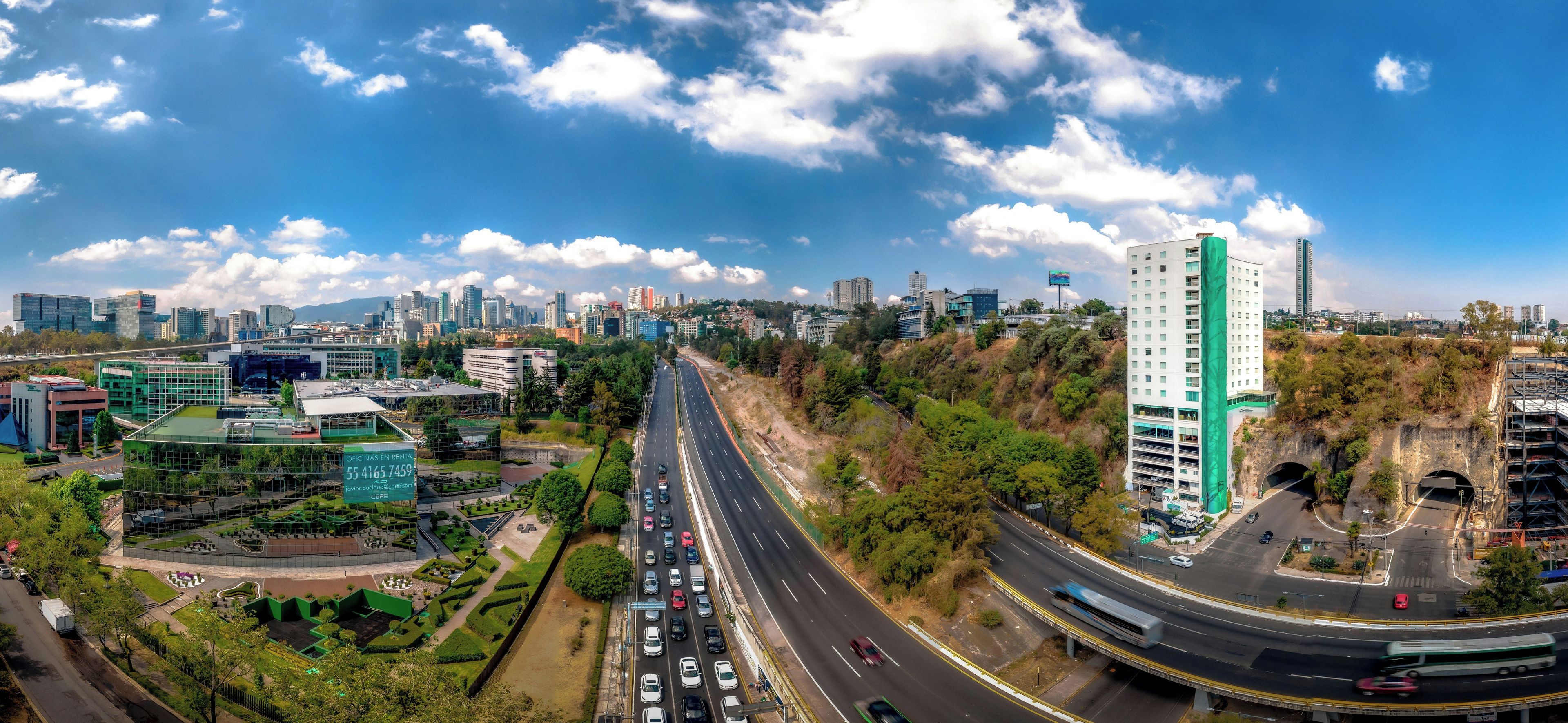 Un paysage urbain comprenant une autoroute, des immeubles et un espace vert traversé par une route.