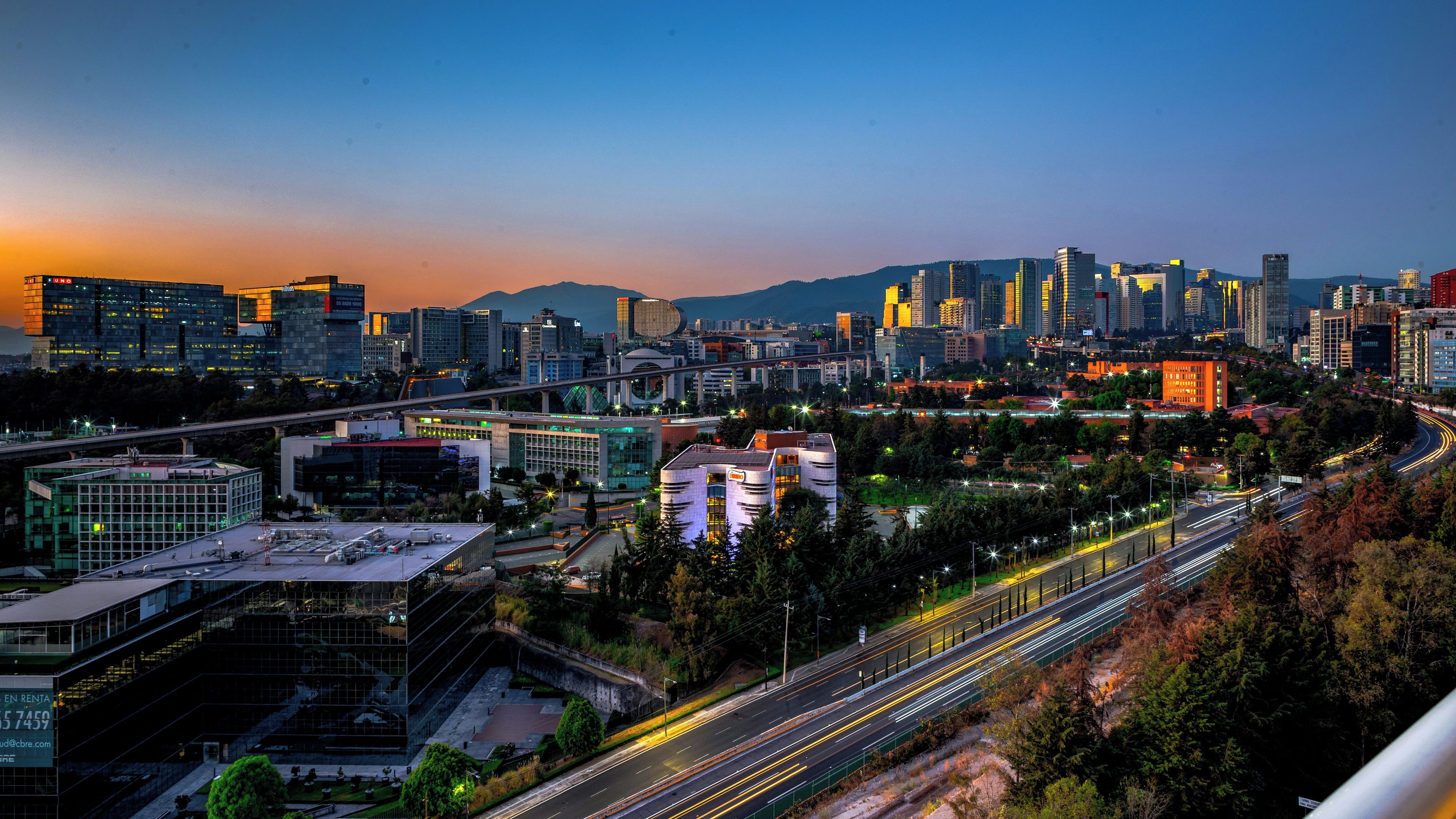 Un paisaje urbano con edificios modernos, una autopista y una montaña al fondo.