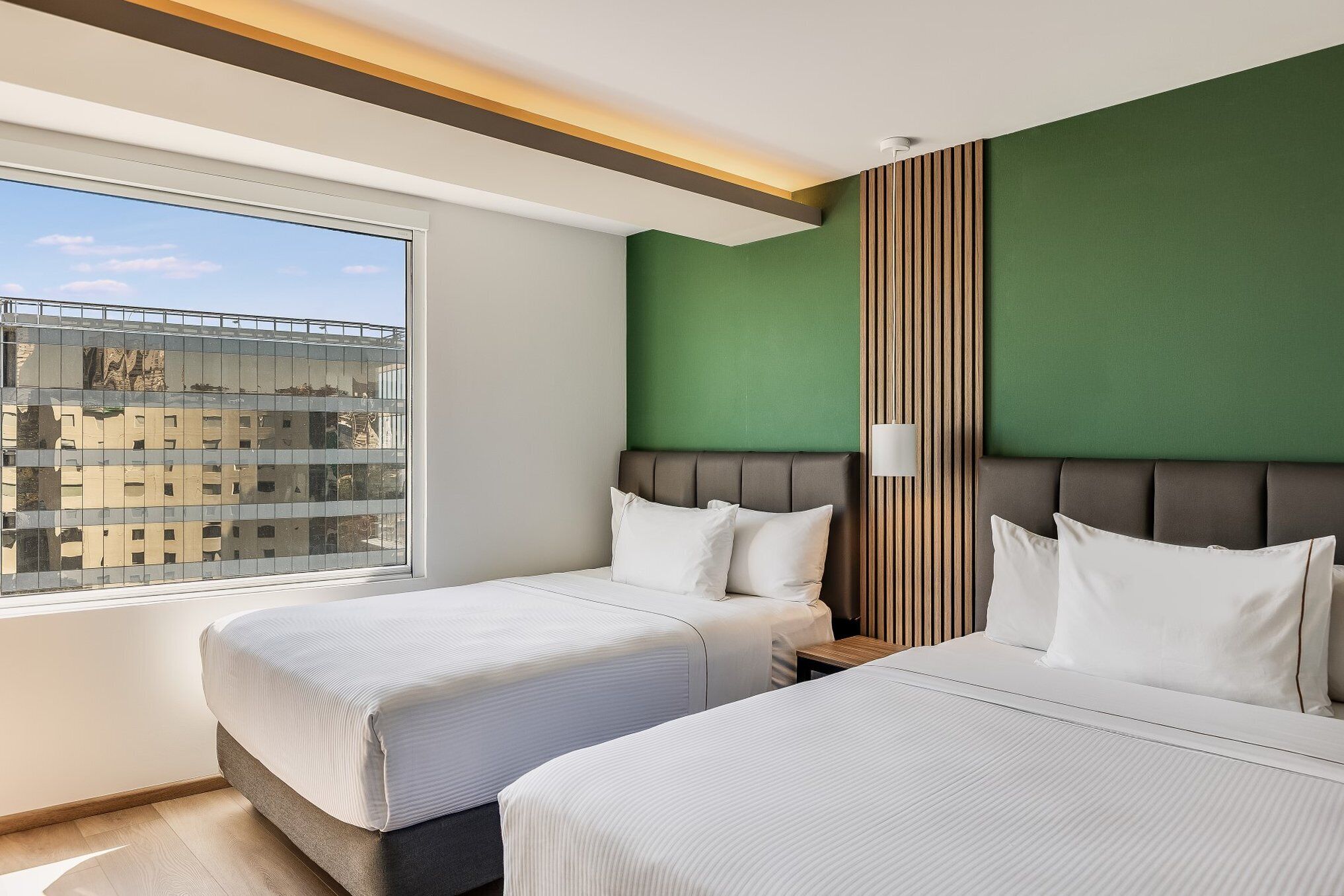 Habitación de hotel con dos camas, un ventanal grande y una pared de acento verde.
