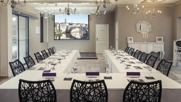 A conference room with a long table, black chairs, chandeliers, a cityscape view, and a white door labeled 'PRIVE.'