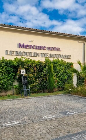 The exterior of Mercure Hotel Le Moulin de Madame with a cobblestone entrance and a lush green hedge.