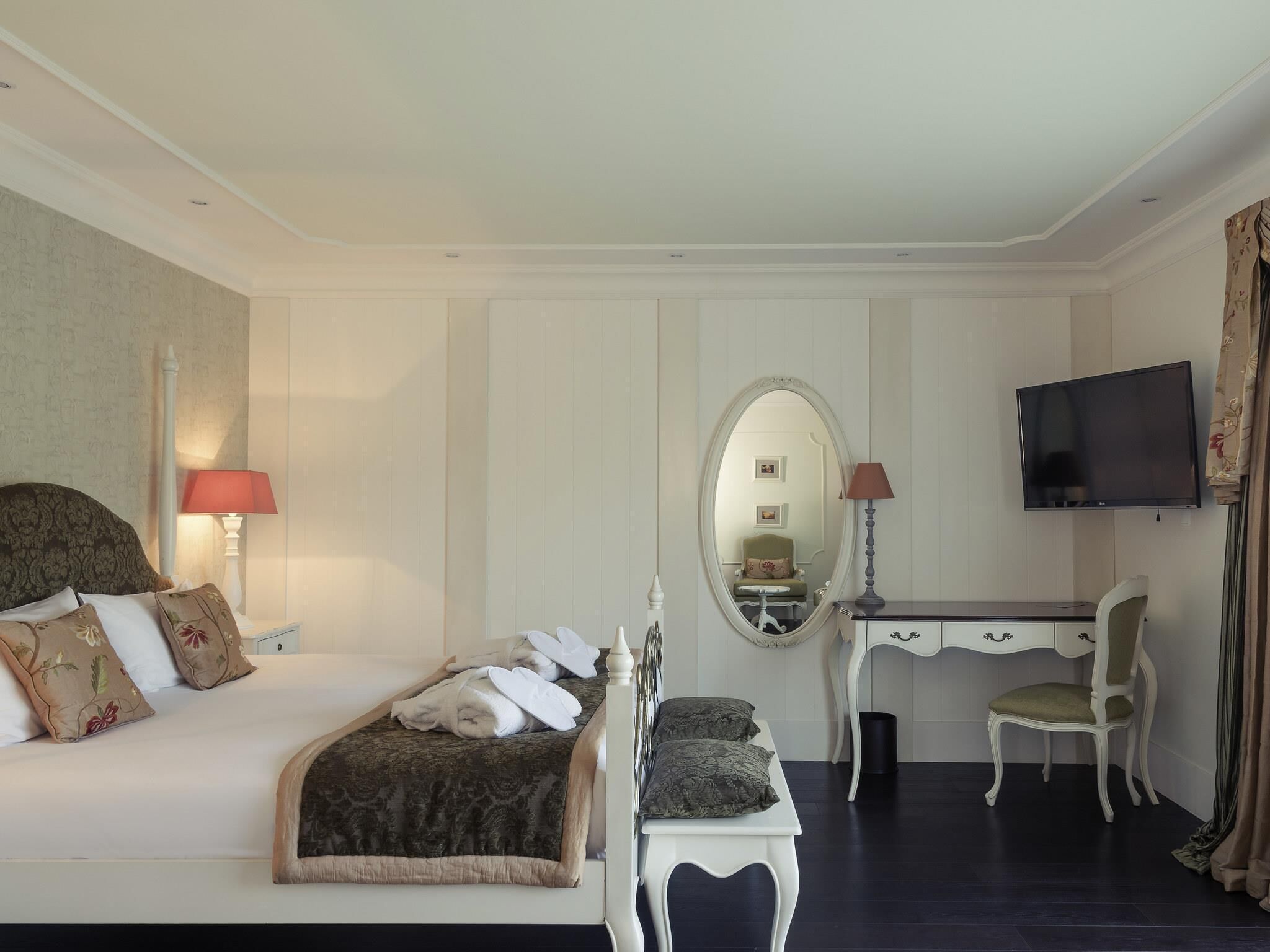 Ein Hotelzimmer mit Bett, Schreibtisch, Stuhl, Fernseher und Spiegel.