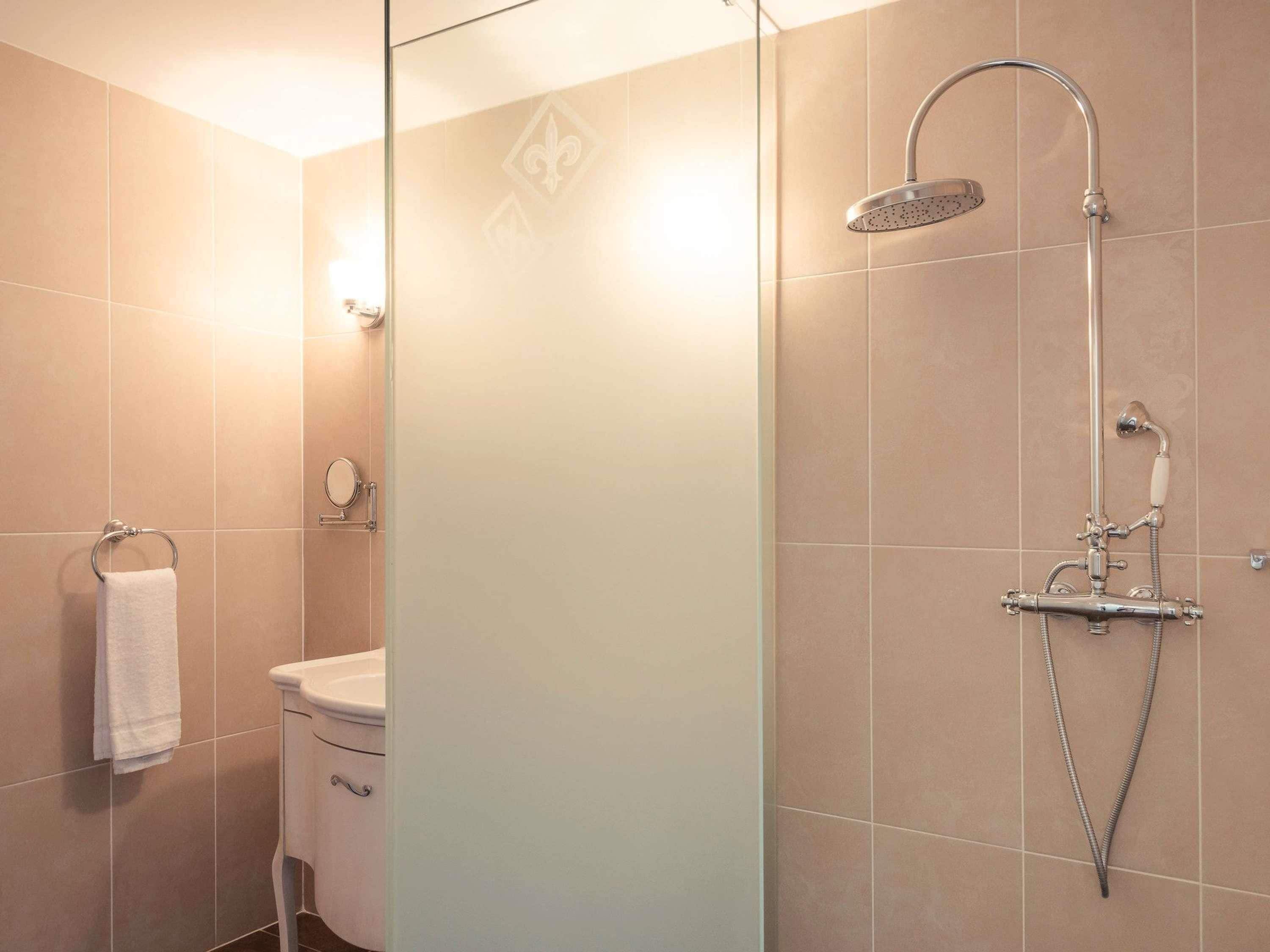 Un baño moderno con mampara de vidrio, ducha con cabezal de ducha de mano, inodoro y toallero.